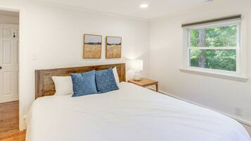 A bedroom with a large bed, a wooden headboard, two wall-mounted paintings, a bedside lamp, and a window with a view of trees.