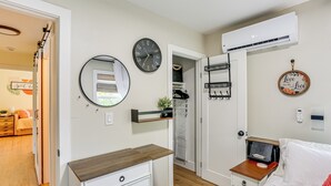 A bedroom with a wooden dresser, a bed with a red blanket, a wall clock, a mirror, an air conditioning unit, and a shelf with a plant. - Walkable & Bright Bungalow in Dtwn Redding! (Redding)