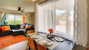 A dining area with a table set for two, a sofa with cushions, a ceiling fan, and a window with sheer curtains. - Walkable & Bright Bungalow in Dtwn Redding! (Redding)