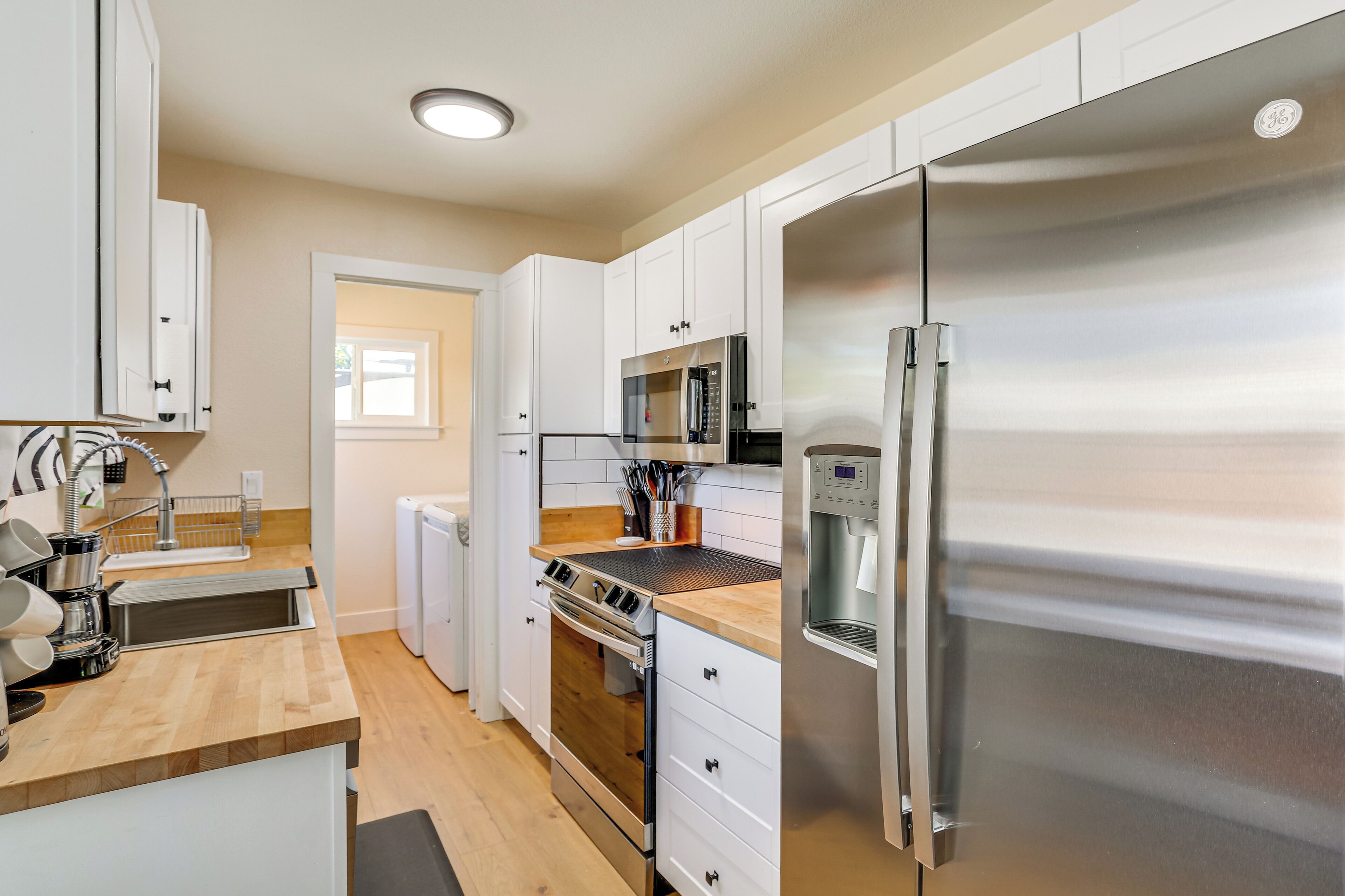 A modern kitchen with white cabinets, stainless steel appliances, a wooden countertop, and a built-in oven.