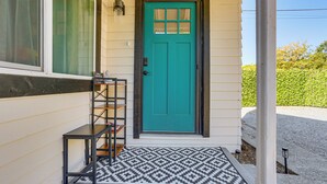 A teal door with a window above it, a black metal shelf, and a patterned rug on a concrete porch. - Walkable & Bright Bungalow in Dtwn Redding! (Redding)