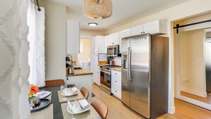 A modern kitchen with white cabinets, a stainless steel refrigerator, and a dining area with a table set for two. - Walkable & Bright Bungalow in Dtwn Redding! (Redding)