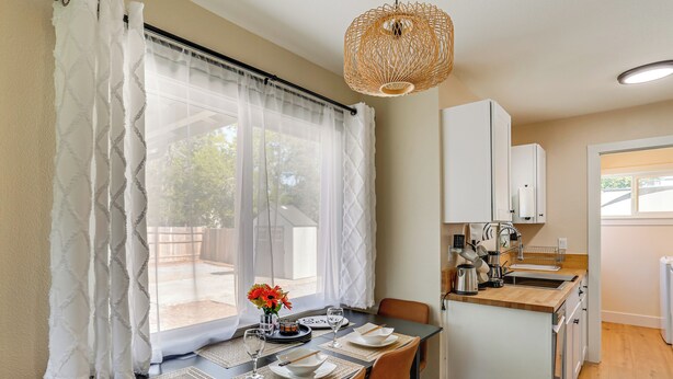 A dining area with a table set for four, a kitchen with white cabinets, and a wicker ceiling light. - Walkable & Bright Bungalow in Dtwn Redding! (Redding)