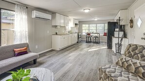 Une cuisine moderne avec des meubles blancs, un coin repas avec une table et des chaises, et un salon avec un canapé et une table basse.