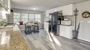 Une cuisine moderne avec des meubles blancs, un réfrigérateur en acier inoxydable, un four à micro-ondes et un coin repas comprenant une table et des chaises.