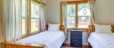 A bedroom with two beds, wooden headboards, a dresser, and a large window with curtains.