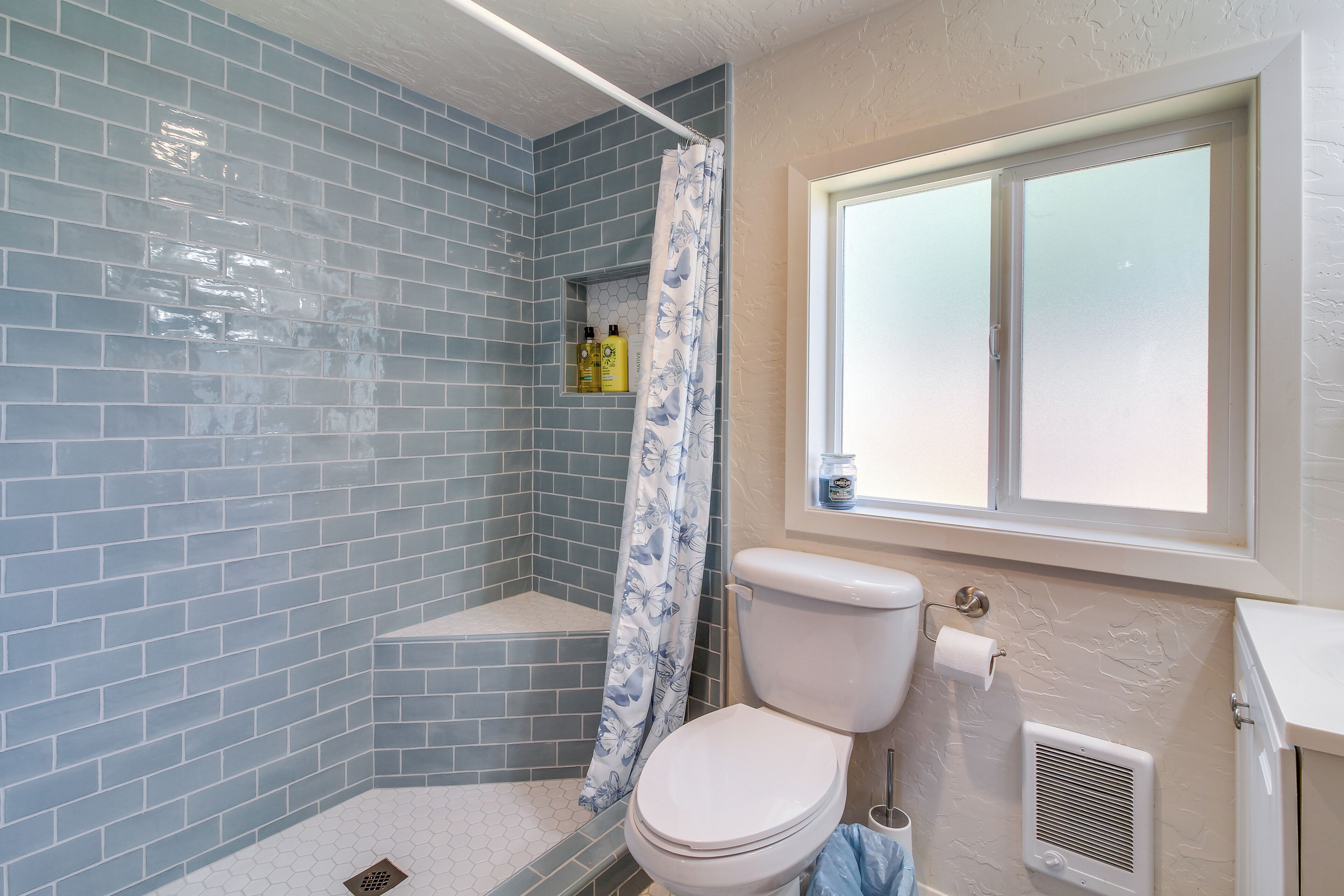 A bathroom with blue-tiled walls, a shower, a toilet, and a window.
