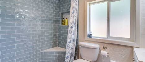 A bathroom with blue-tiled walls, a shower, a toilet, and a window.