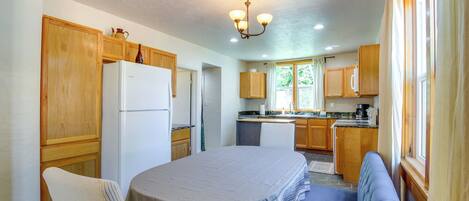 A kitchen with wooden cabinets, a refrigerator, a dining table with a bench, and a window with curtains.
