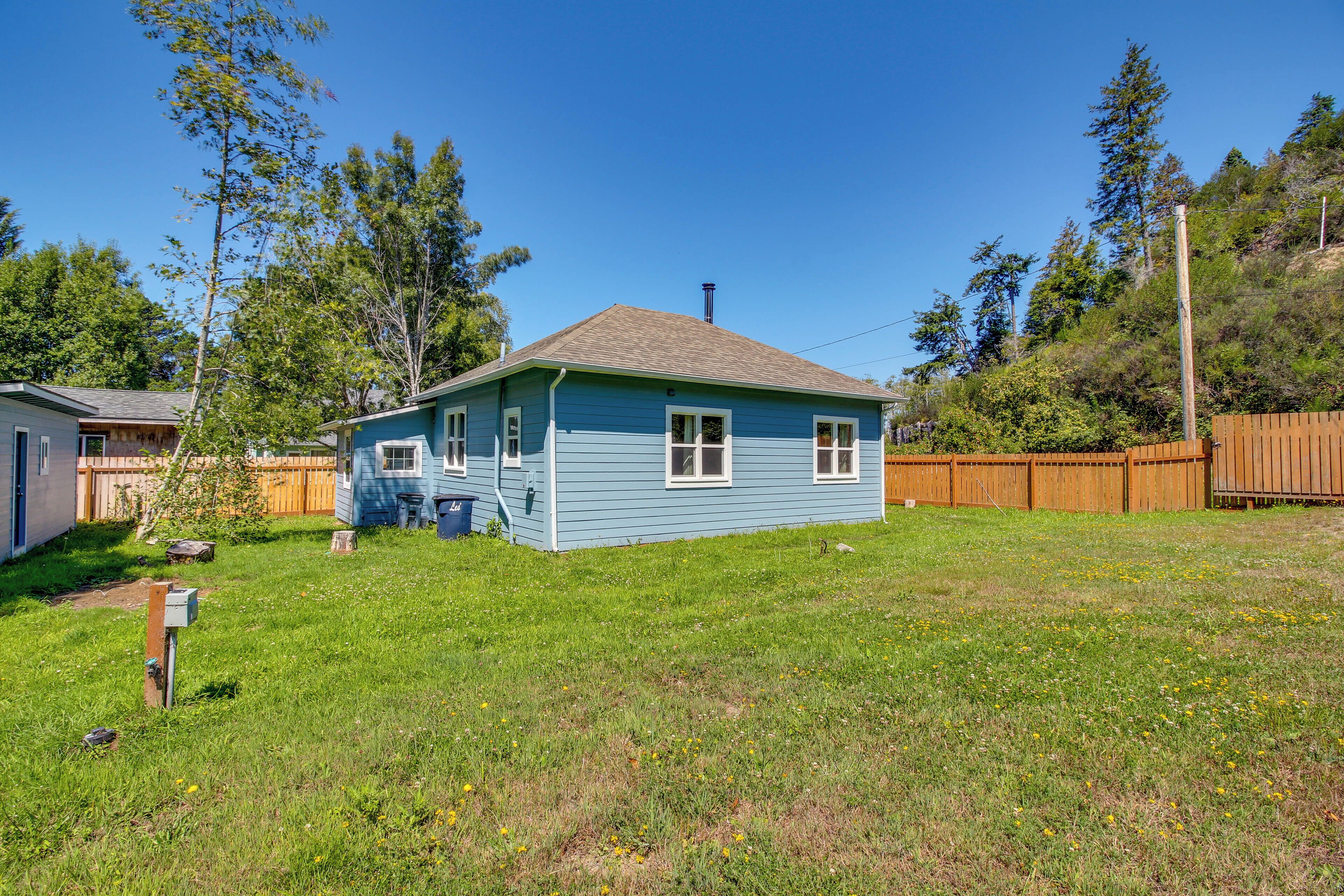 A single-story house with a blue exterior and a sloped roof, surrounded by a wooden fence and a grassy yard.