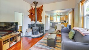 Una sala de estar con un televisor de pantalla plana grande, un sofá, un mueble de entretenimiento de madera, una chimenea de piedra y una cocina al fondo.