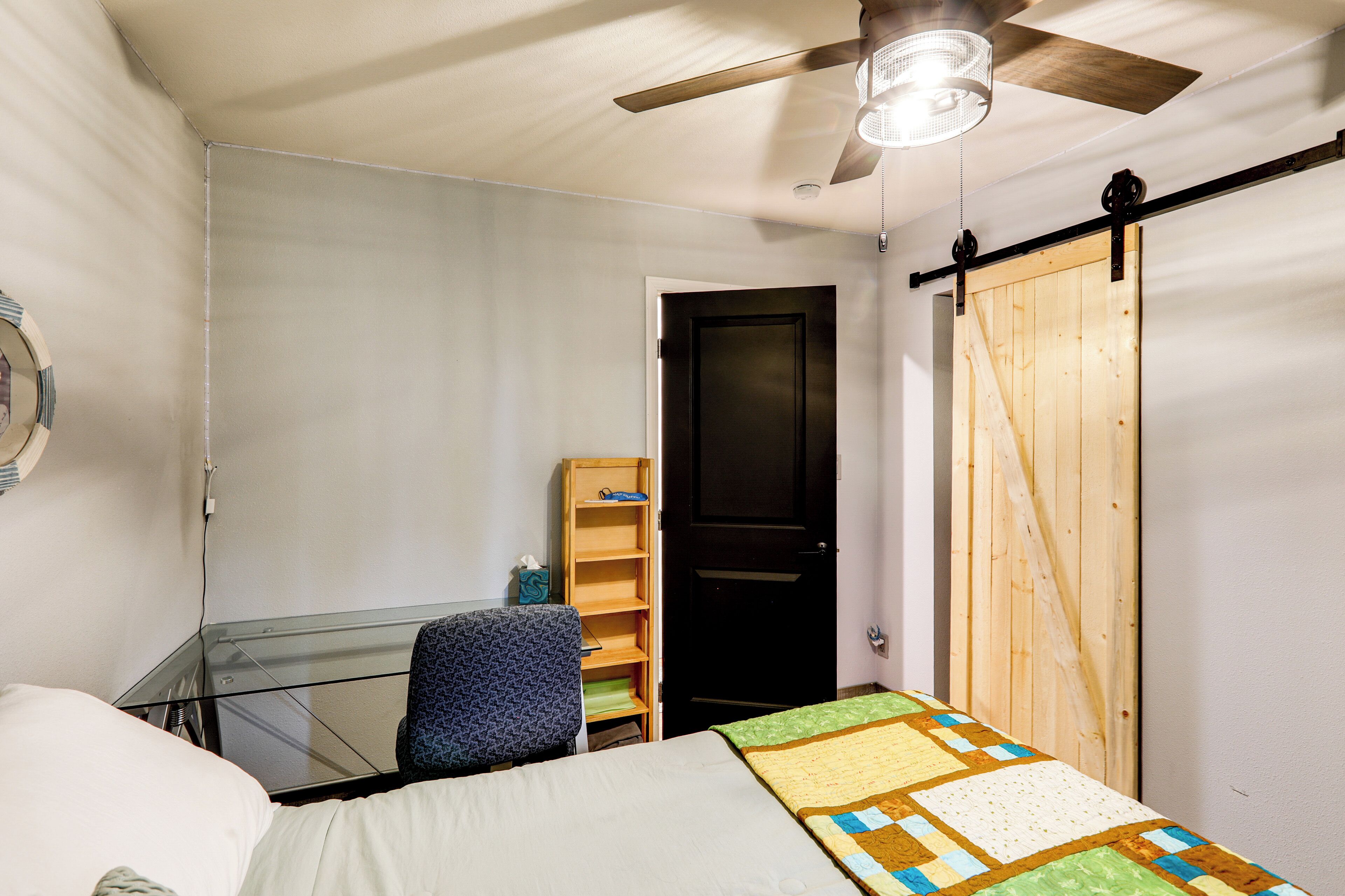 A bedroom with a bed, a desk, a chair, a wardrobe, and a ceiling fan.