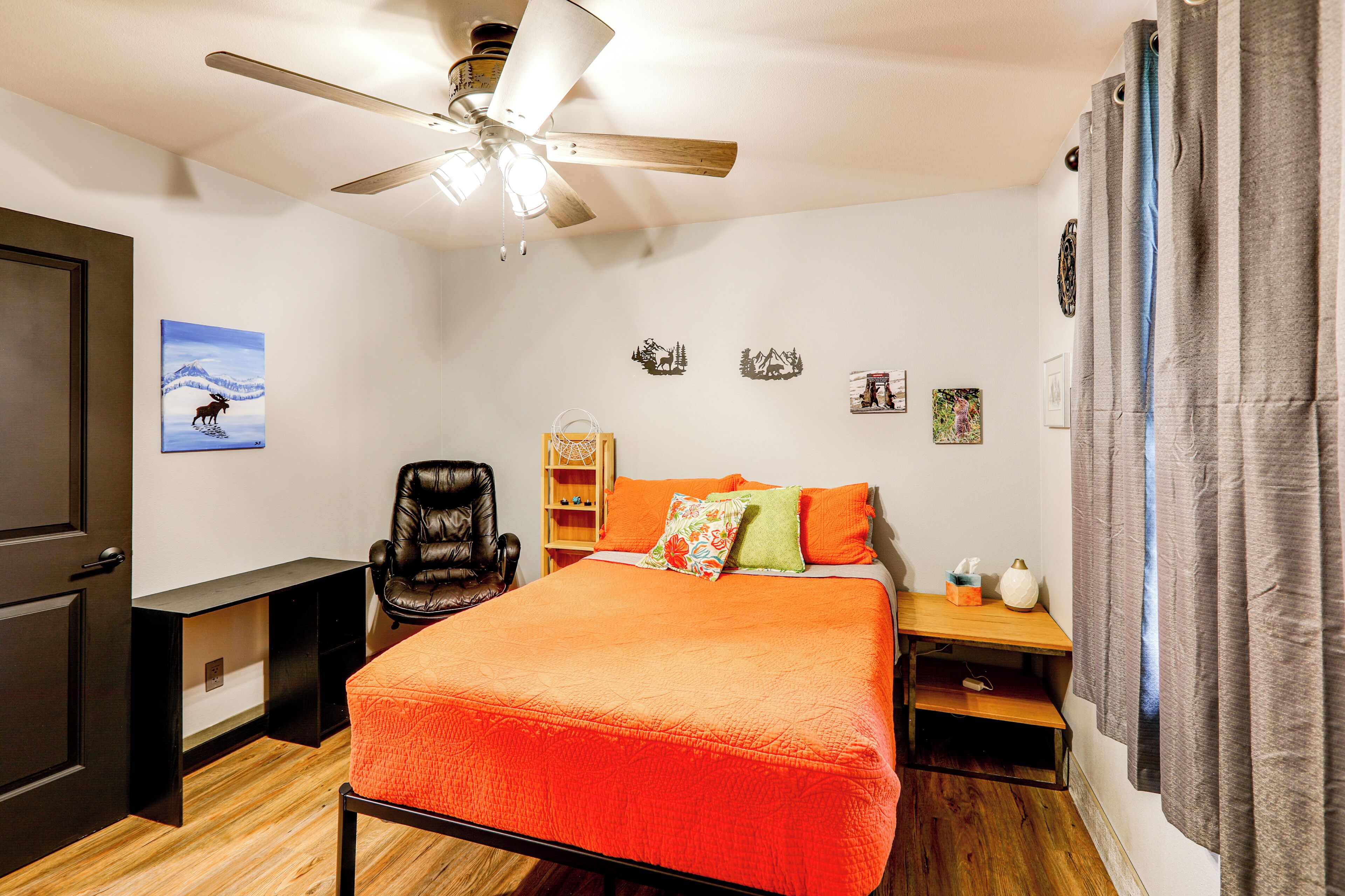 A bedroom with a bed, a desk, a chair, a ceiling fan, and a nightstand.