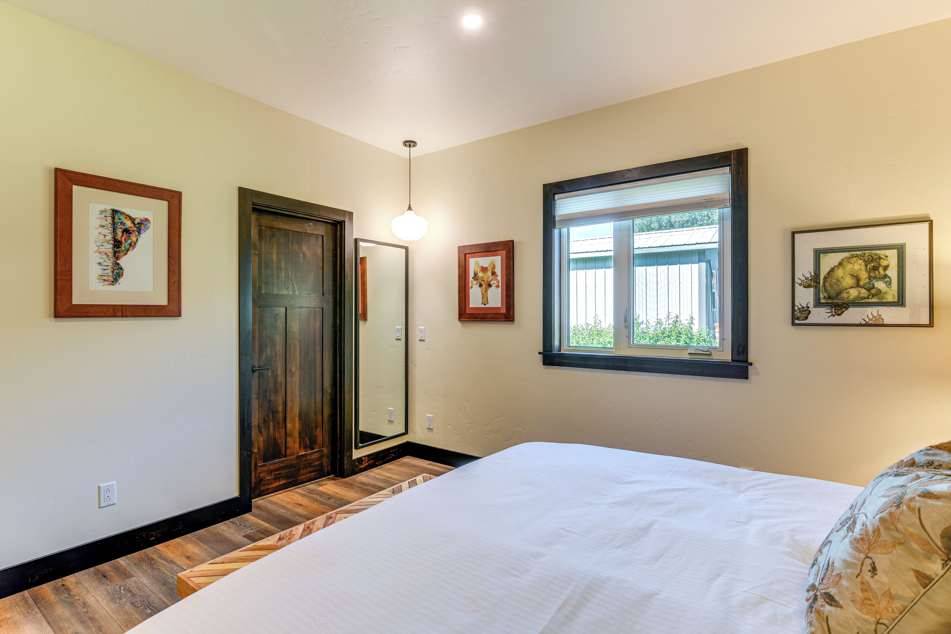 Un dormitorio con una cama grande, suelo de madera, una ventana con persianas y cuadros en las paredes.
