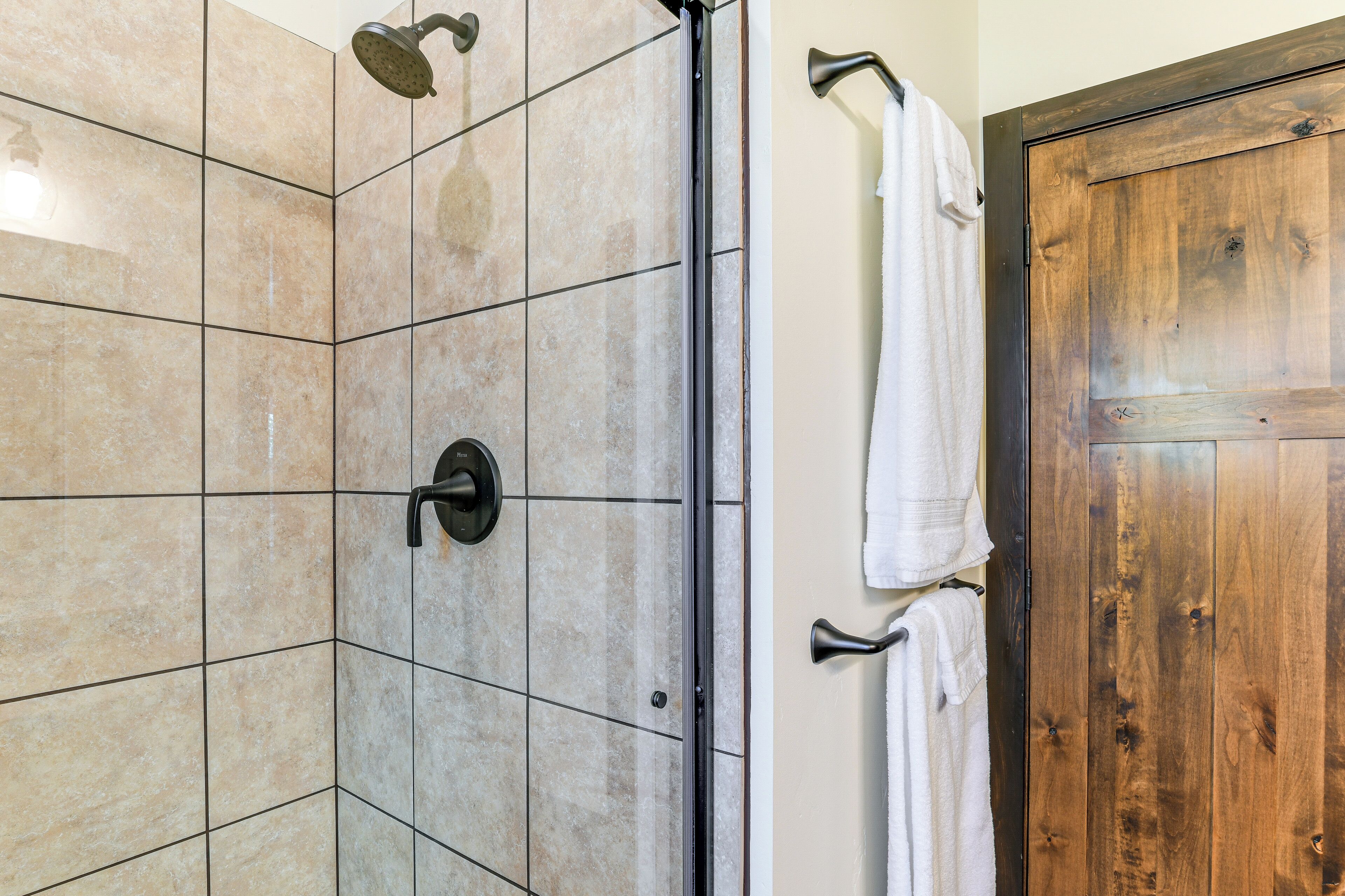 A bathroom with a shower area, tiled walls, and a wooden door.