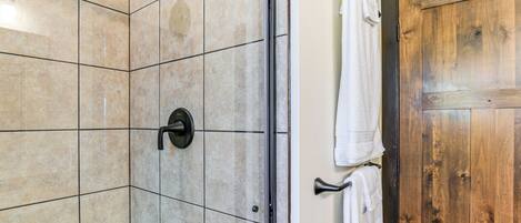 A bathroom with a shower area, tiled walls, and a wooden door.