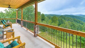 Eine Holzterrasse mit Gartenmöbeln und einer Stein Säule, mit Blick auf eine bewaldete Berglandschaft.