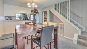 A dining area with a wooden table, chairs, and a vase of flowers. There is a staircase with a railing leading to a landing. - Norcross Townhome ~ 18 Mi to Dtwn Atlanta! (Norcross)
