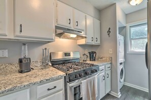 Une cuisine avec des meubles blancs, une cuisinière à gaz, un mixeur et un lave-linge.