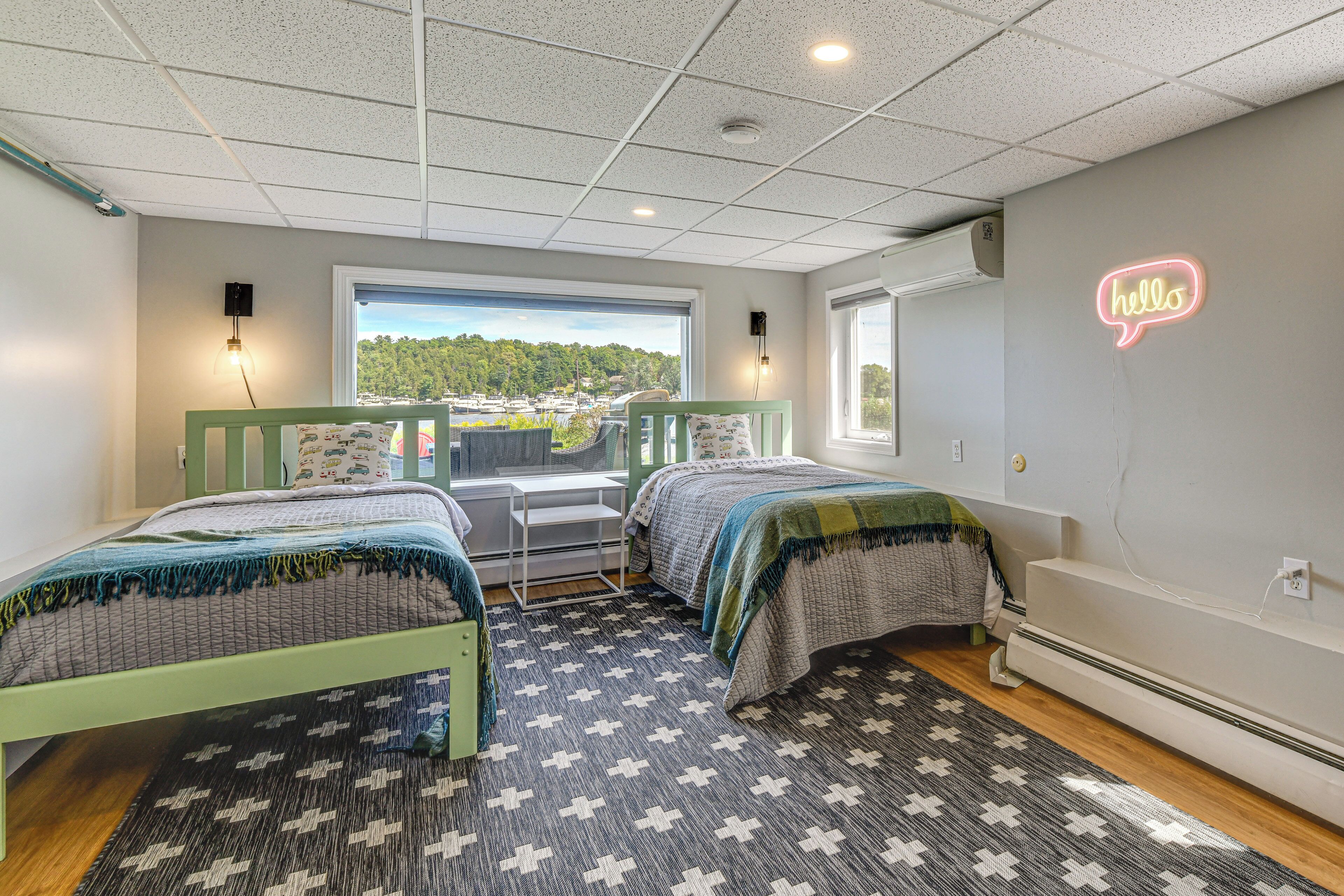 Une chambre avec deux lits, une vue sur l’extérieur et un néon représentant le mot « bonjour » accroché au mur.