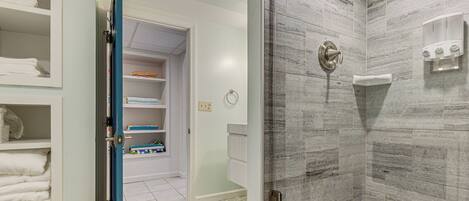 A bathroom with a shower, a towel rack, and a storage area with shelves.