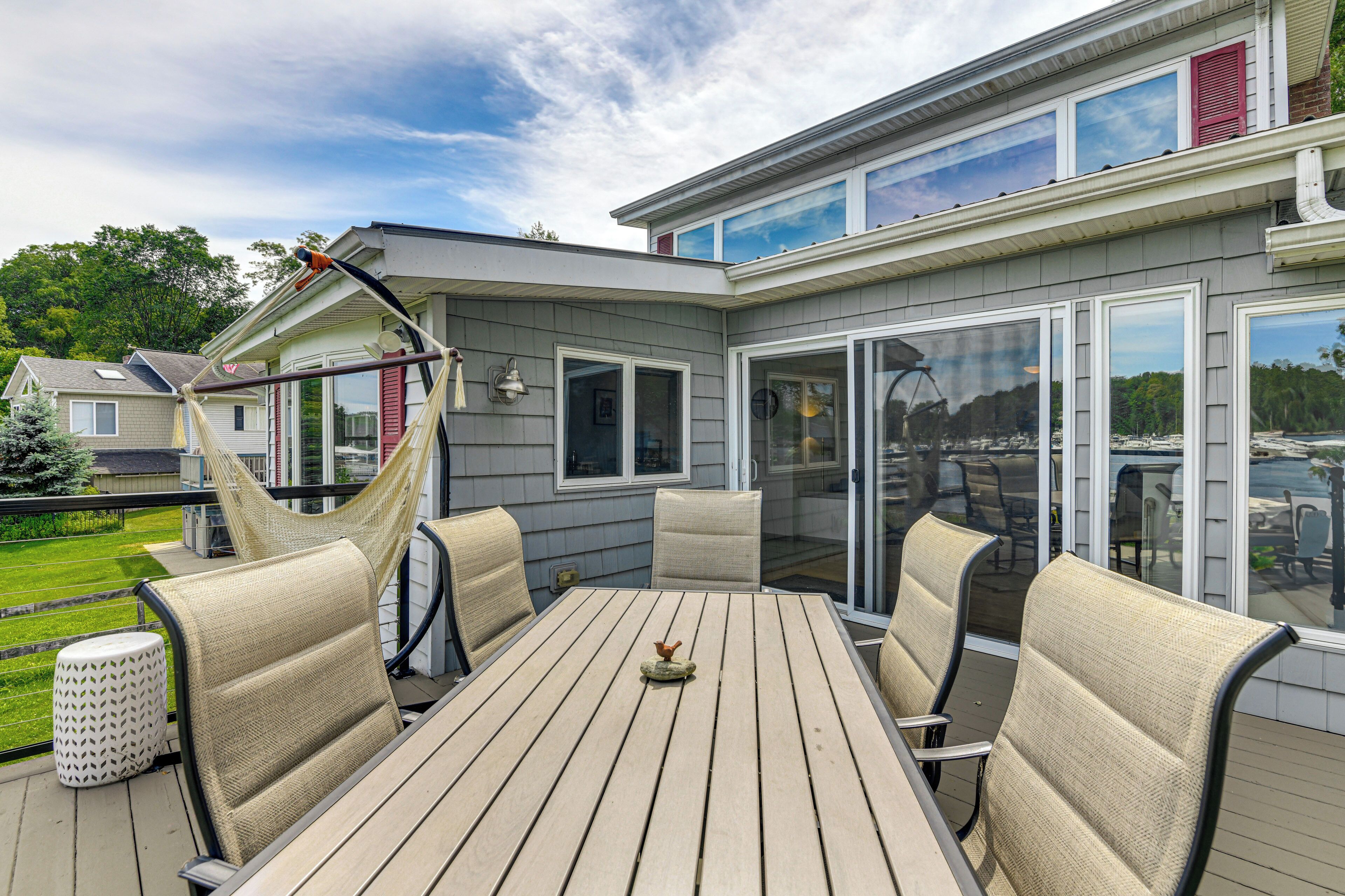 An outdoor patio with a wooden table and chairs, a hammock, and a glass door leading to a deck.