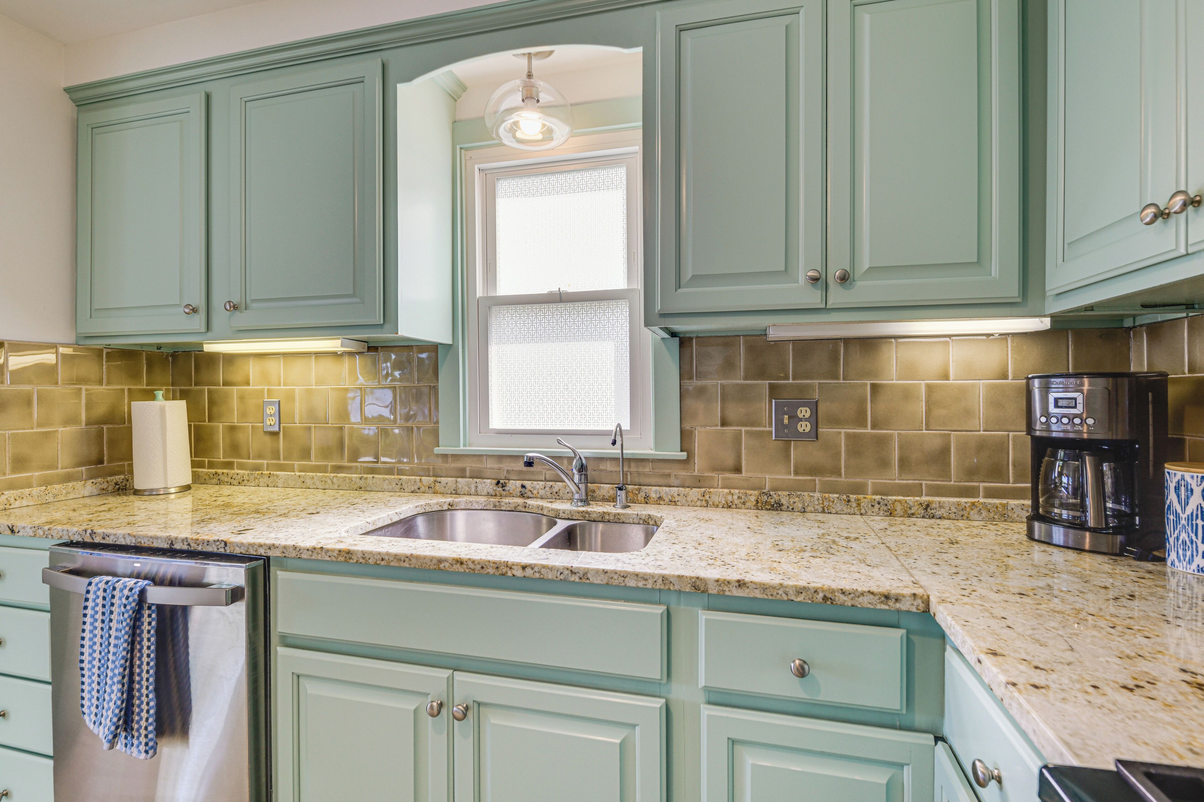 A kitchen with teal cabinets, a granite countertop, a double sink, and a coffee maker.