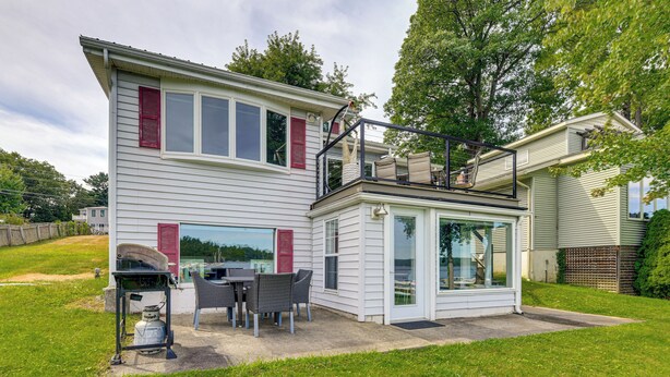 Una casa de dos pisos con un balcón, un patio con mobiliario exterior y un ventanal grande.