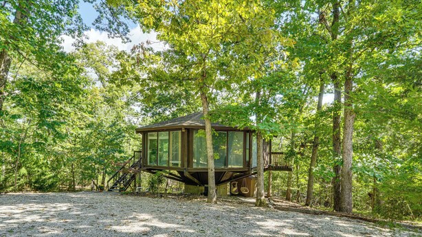 A treehouse with a wooden exterior and a gravel ground.