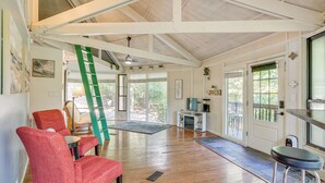 A spacious room with wooden floors, a red chair, a green ladder, and a TV on a white stand.