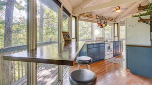 A kitchen with a large window overlooking a forest, wooden flooring, and a bar area with stools.