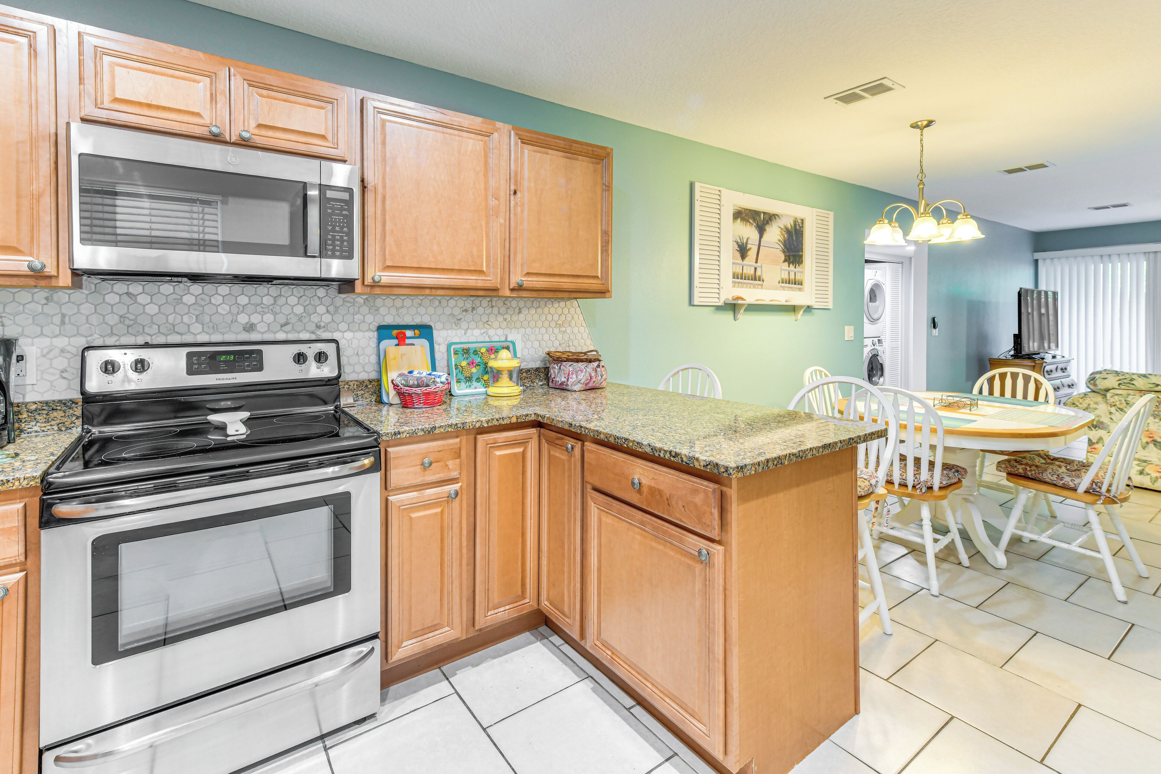 A kitchen with wooden cabinets, a stainless steel stove, and a microwave. There is a dining area with a table and chairs.