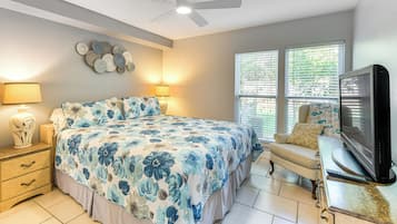 A bedroom with a large bed, a TV, a chair, and a ceiling fan.