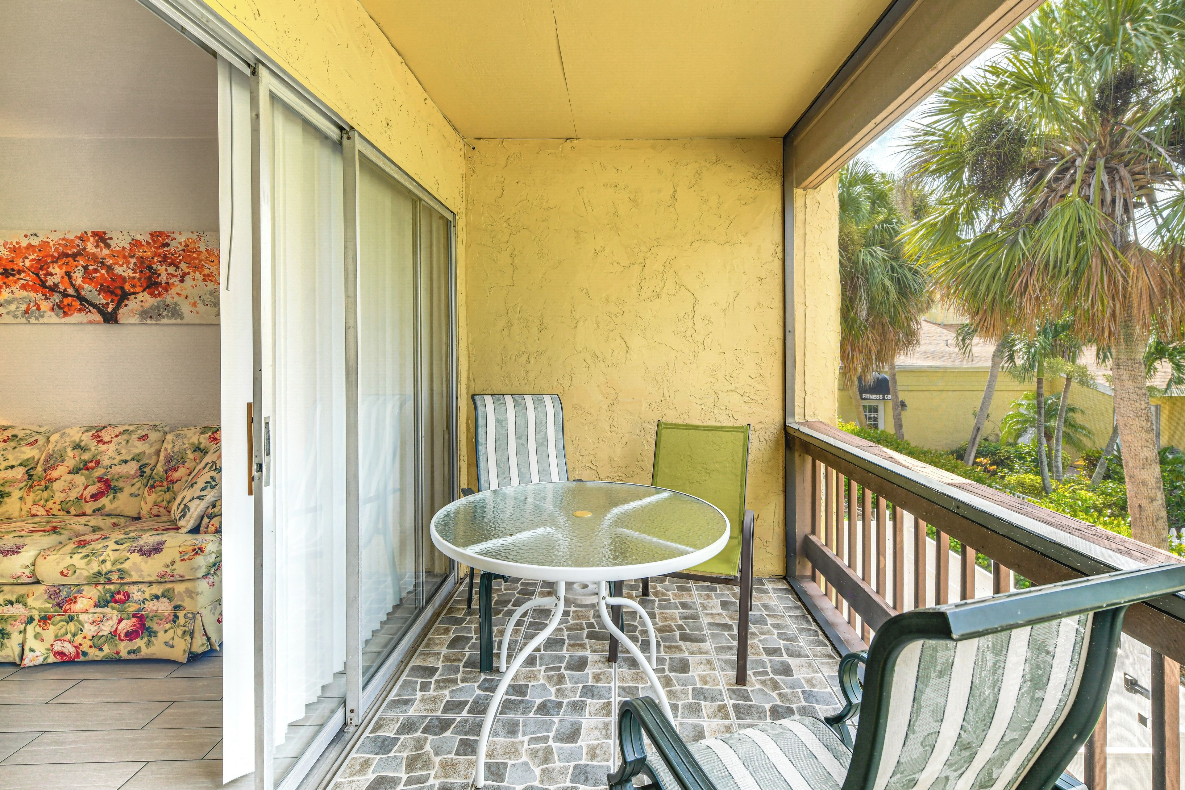 A balcony with a glass table, a striped chair, and a floral sofa.