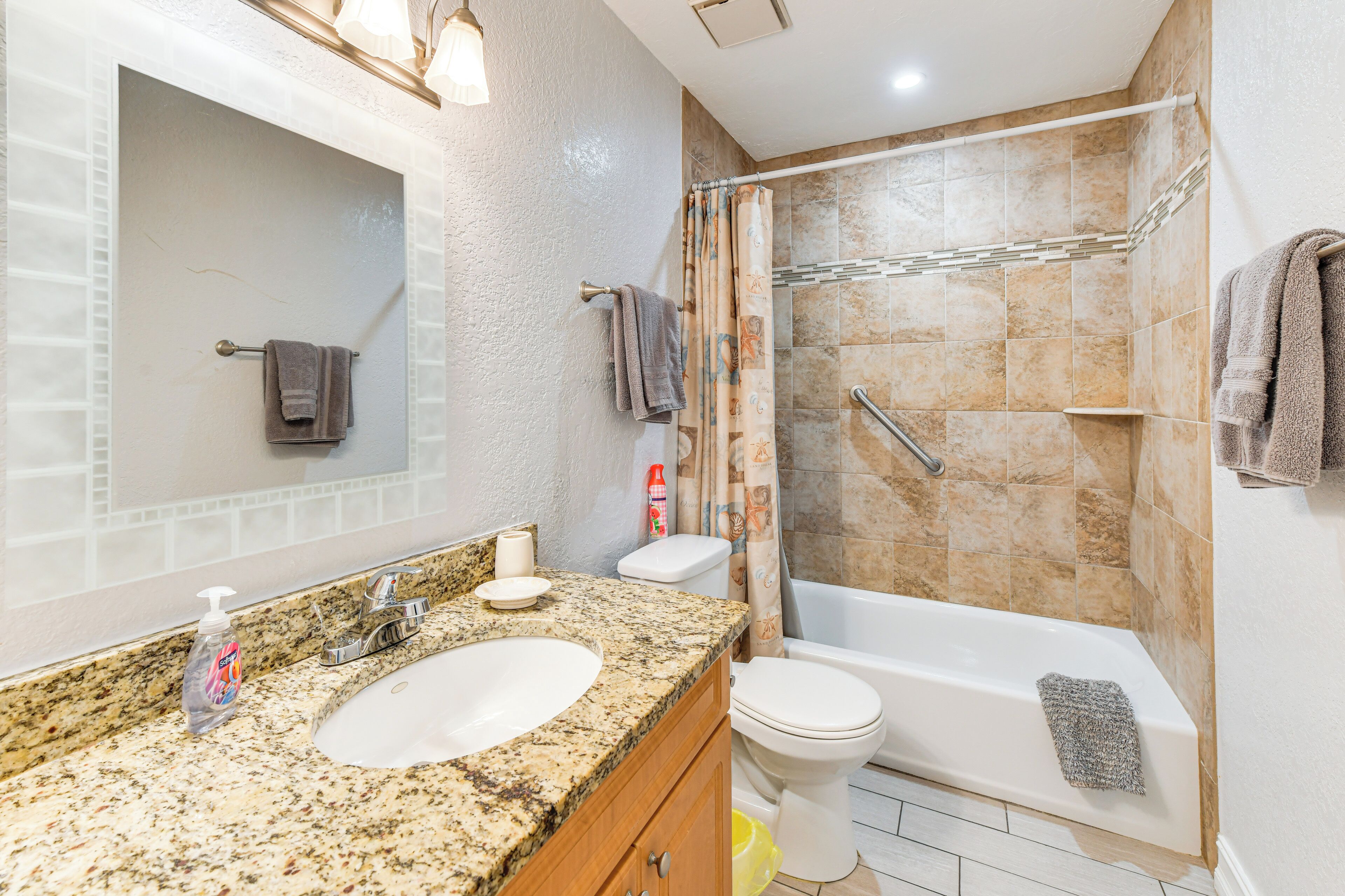 A bathroom with a granite countertop sink, a toilet, a bathtub, and a shower with a curtain.