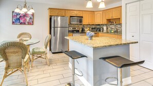 Une cuisine moderne avec des meubles en bois, des appareils électroménagers en acier inoxydable, un plan de travail en granit et un coin repas avec des chaises et une table en osier.