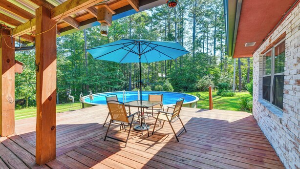 A wooden deck with a pool table and chairs, surrounded by a pool and a brick house. - Pool & Deck: Pond-view Getaway in Newnan! (Newnan)