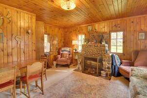 Interior acogedor de una cabaña de madera con chimenea de piedra, mesa de comedor de madera y asientos cómodos.