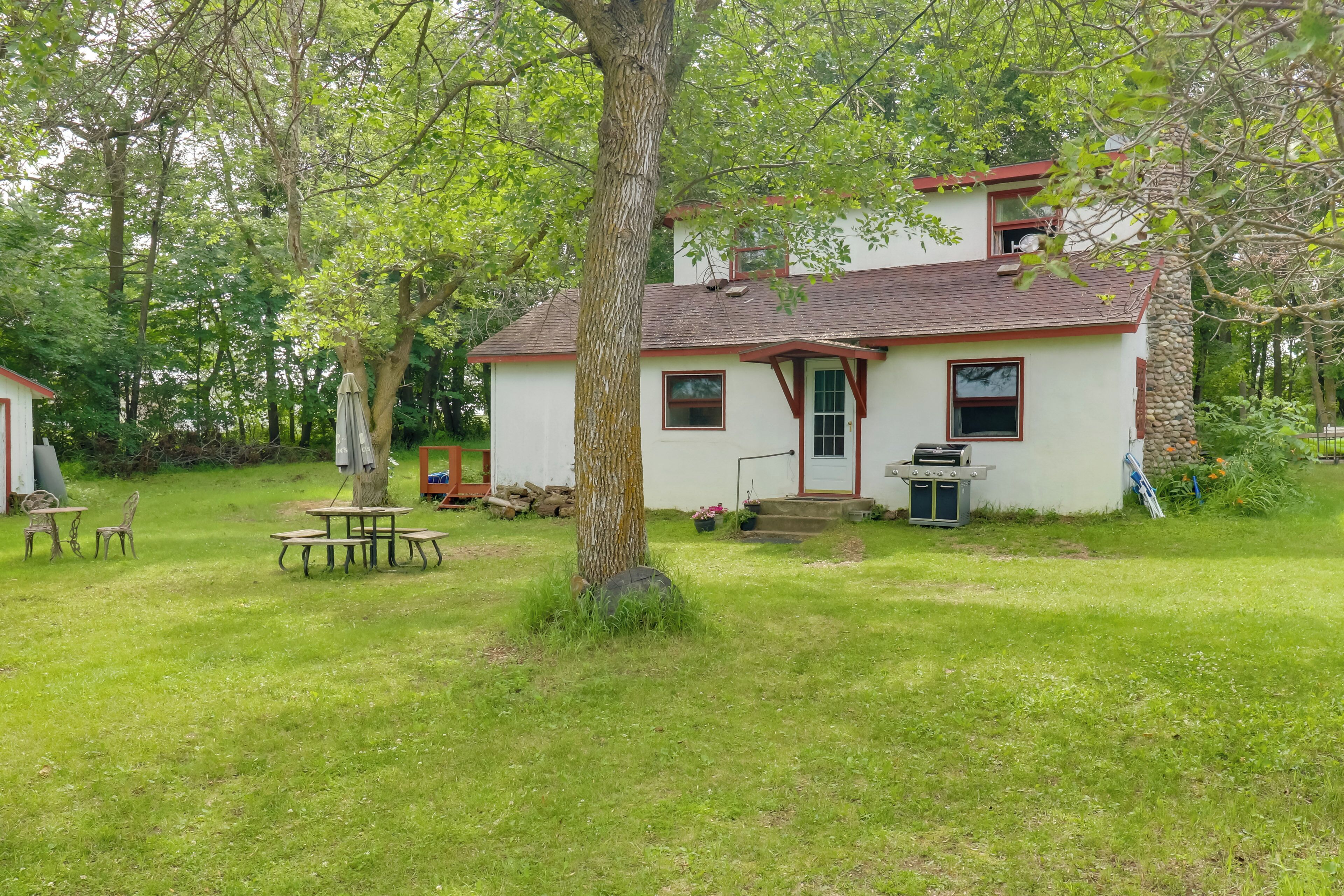 A house with a red roof and white walls, surrounded by a grassy yard and trees.