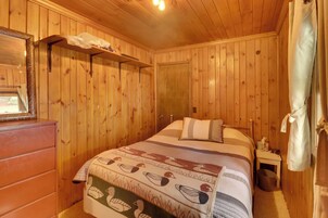 Una habitación con paneles de madera, una cama, un tocador y una pequeña mesa.