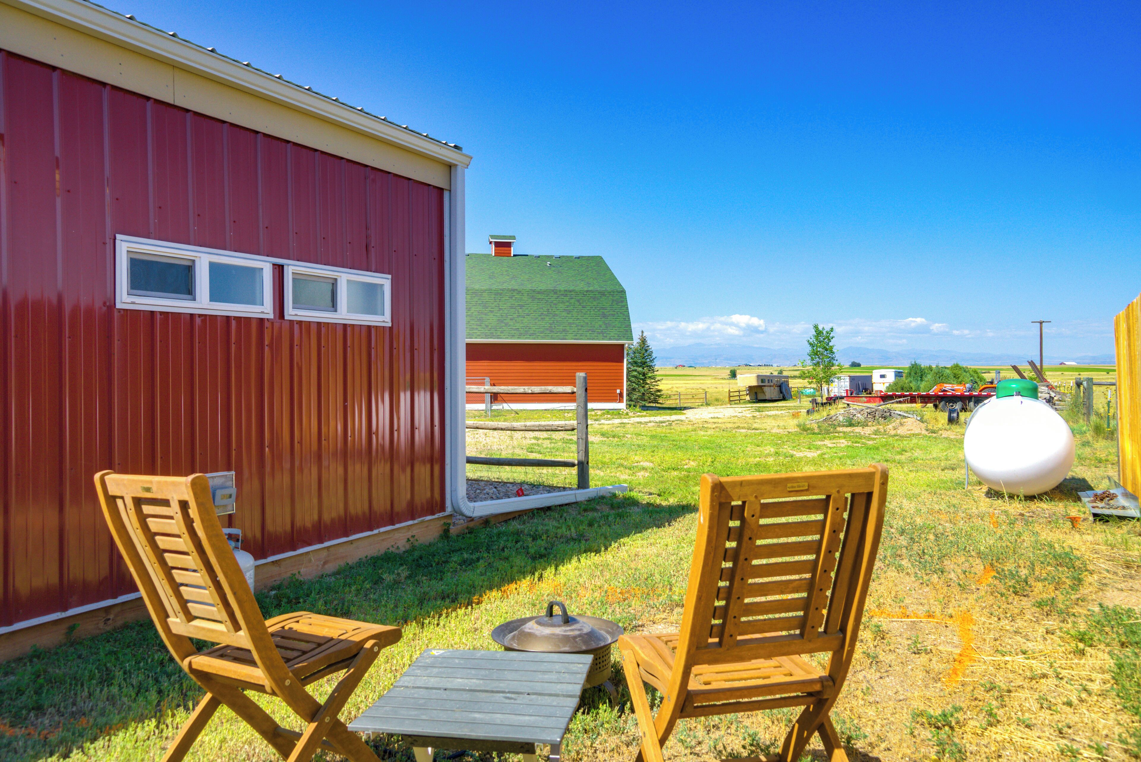 A red barn with two wooden chairs and a table outside.