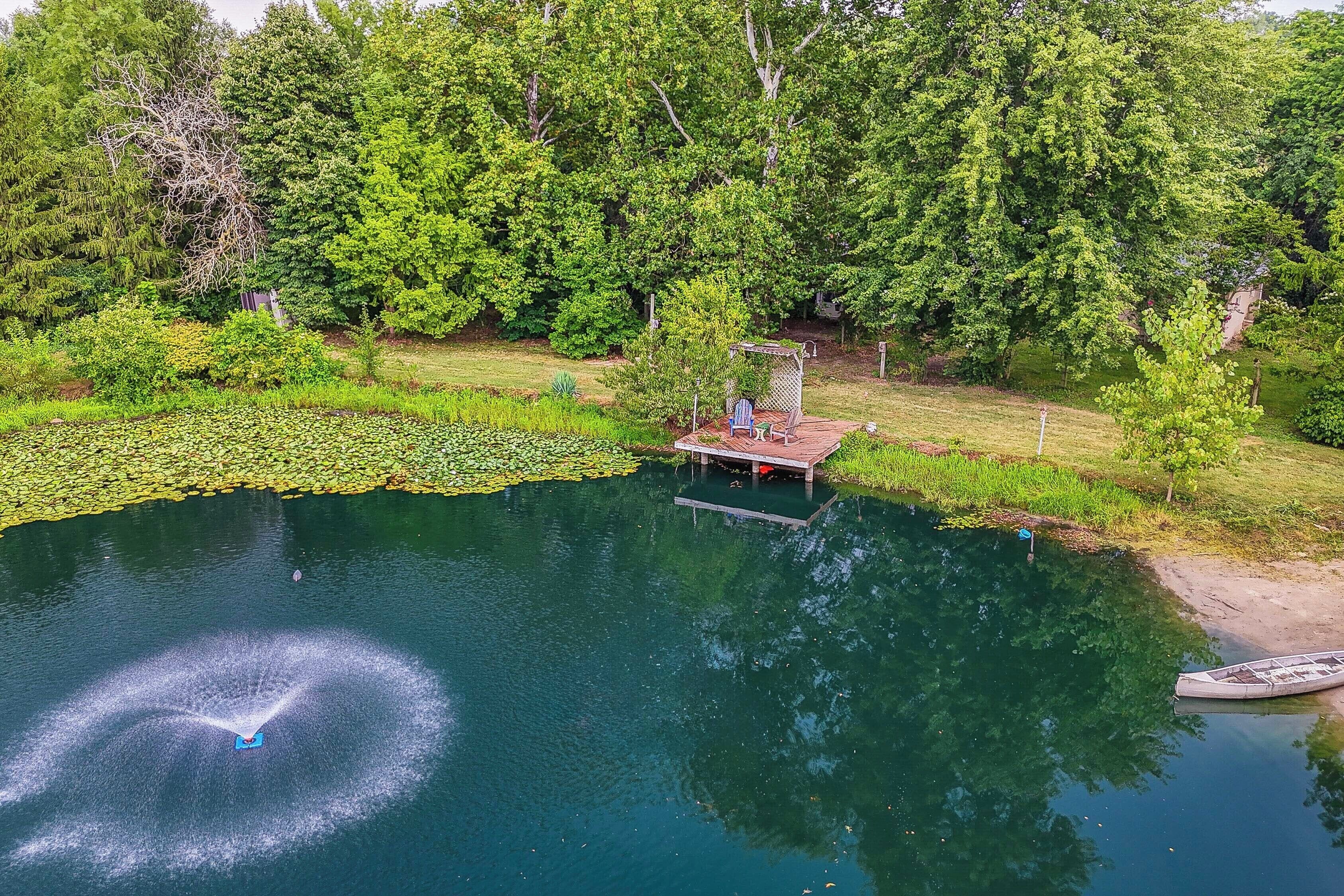 A serene lakeside setting with a wooden dock extending into the water, surrounded by lush greenery and trees.