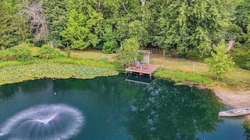 A serene lakeside setting with a wooden dock extending into the water, surrounded by lush greenery and trees.