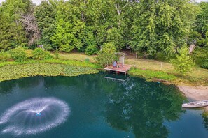 A serene lakeside setting with a wooden dock extending into the water, surrounded by lush greenery and trees.