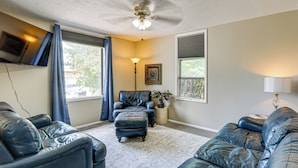 A living room with a ceiling fan, a flat-screen TV mounted on the wall, a leather sofa, a matching ottoman, and a floor lamp.
