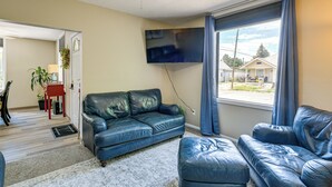A living room with a blue leather sofa, a television mounted on the wall, and a window with curtains.