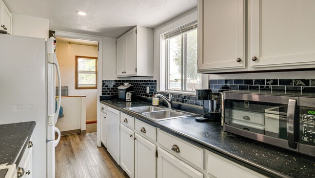 A kitchen with white cabinets, a black countertop, a sink, a microwave, and a window.