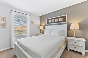 Un dormitorio con cama, mesitas de noche, una ventana con persianas y decoración en la pared.