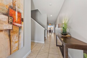 A hallway with a staircase, a dining area in the background, and a plant on a console table.