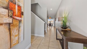 A hallway with a staircase, a dining area in the background, and a potted plant on a console table. - Minutes to Disney•Pvt Pool•Free Wi-Fi & Perks (Kissimmee)